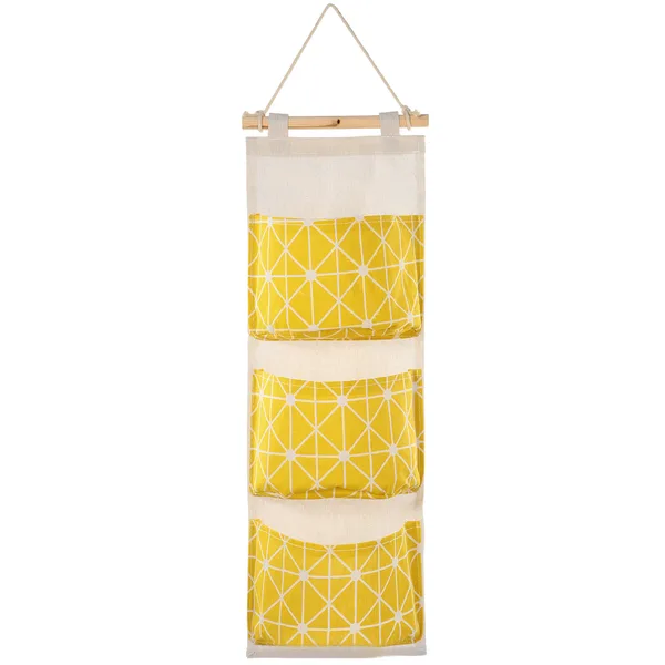 Yellow and white linen-cotton wall organizer with three pockets hanging from a wooden rod by a rope loop. Photo: Sesoris product catalog