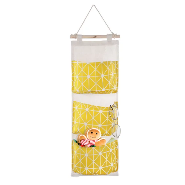 Hanging wall organizer with three yellow fabric pockets on a wooden rod, holding small items. Photo: Sesoris product catalog