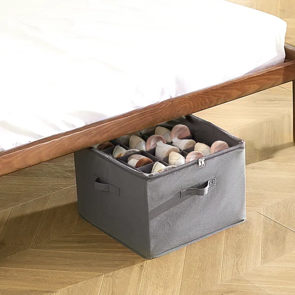 Gray fabric under-bed shoe storage box with a clear zip-top lid, slid partly under a bed frame and holding pairs of shoes in separate compartments. Photo: Sesoris product catalog